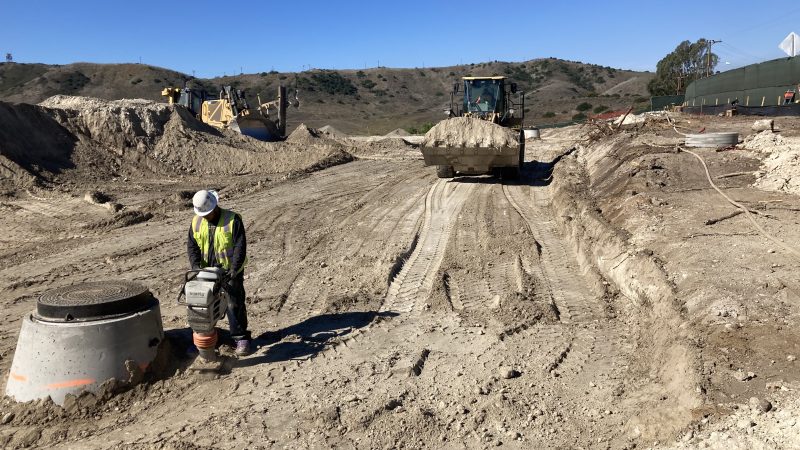 Construction worker in safety gear operates machinery at dusty site.