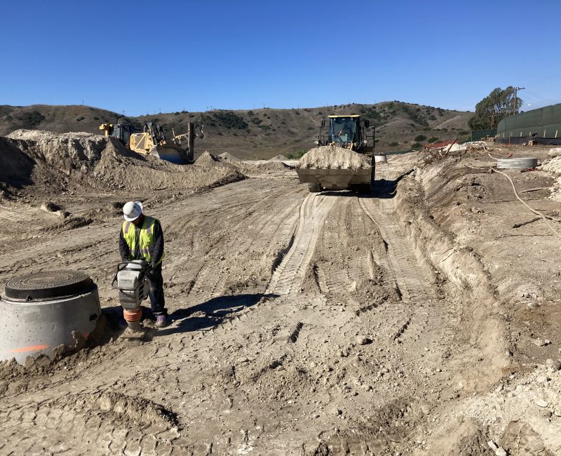 Construction worker in safety gear operates machinery at dusty site.