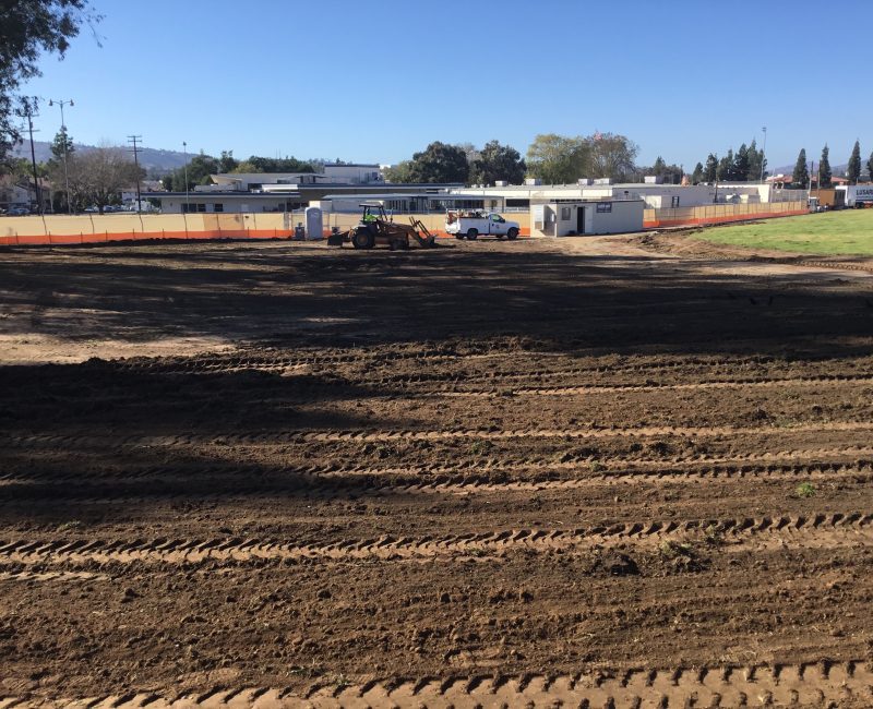 Bulldozer, truck, and tracks on a graded dirt lot.