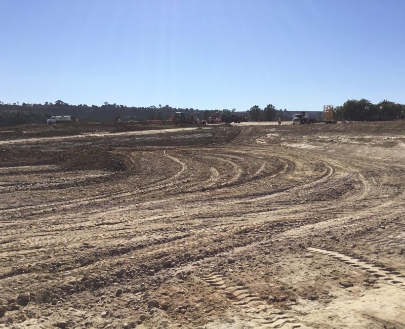 Dusty construction site with tire tracks, equipment, and blue sky.
