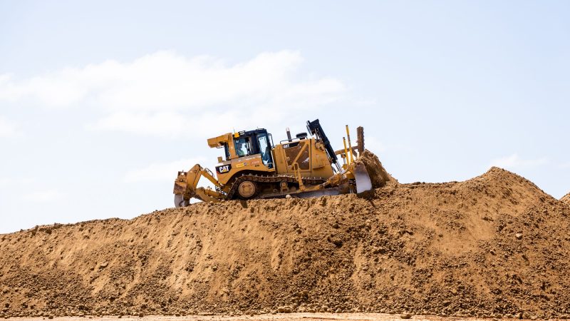 Yellow bulldozer pushes dirt on construction site under blue sky.