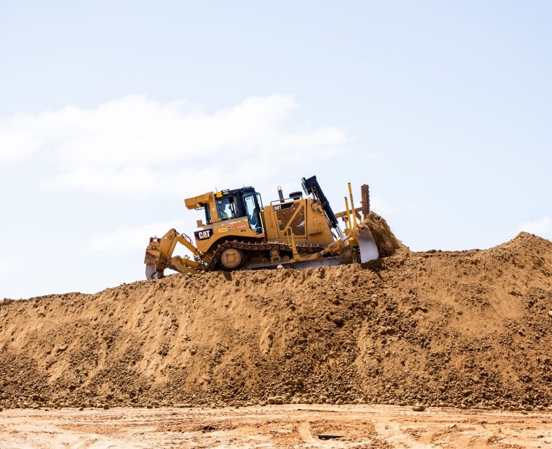 Yellow bulldozer pushes dirt on construction site under blue sky.