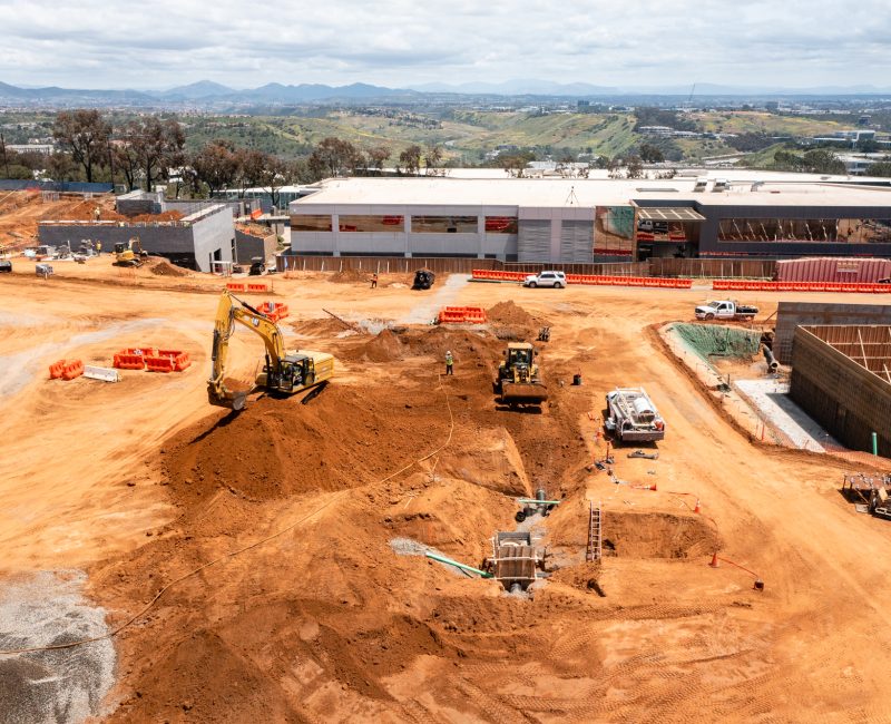 Construction site with machines, materials, half-built structures, and hills.