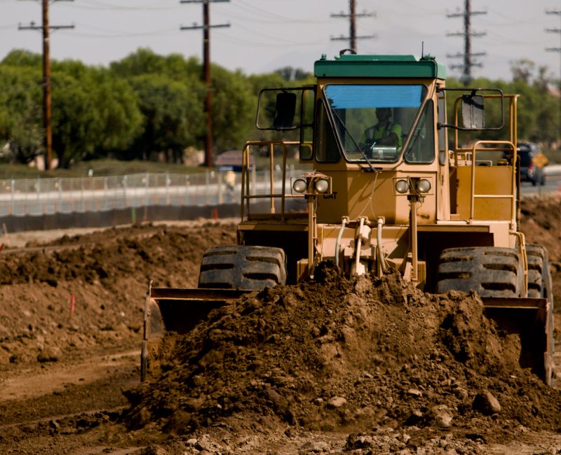 Yellow bulldozer pushes dirt beside a road under cloudy sky.