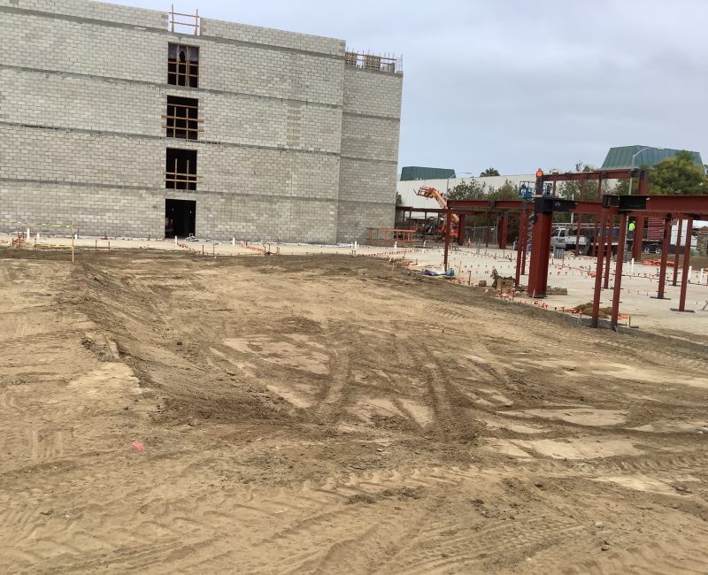 Construction site with dirt, brick building, steel framework, materials.