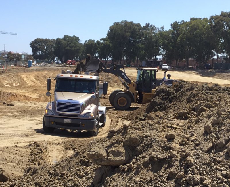 Bulldozer loading dirt into dump truck at construction site.