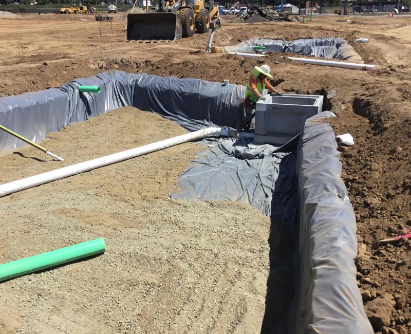 Worker in vest and hat fixes utility box in gravel trench.