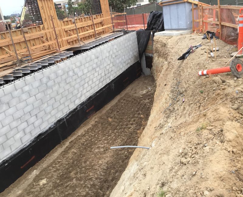 Partially built block wall, deep trench, dirt piles, scattered tools.