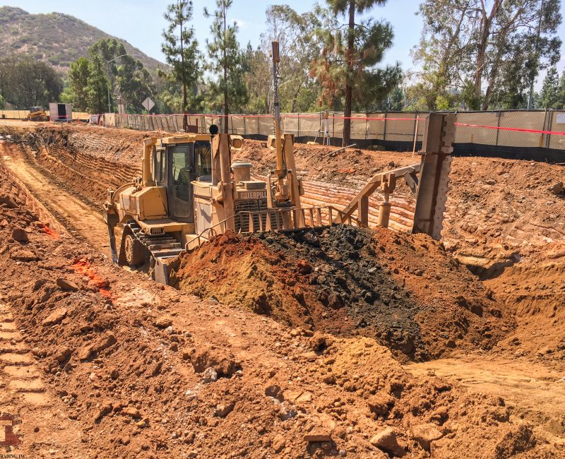 Bulldozer pushes dirt in trench at tree-lined construction site.