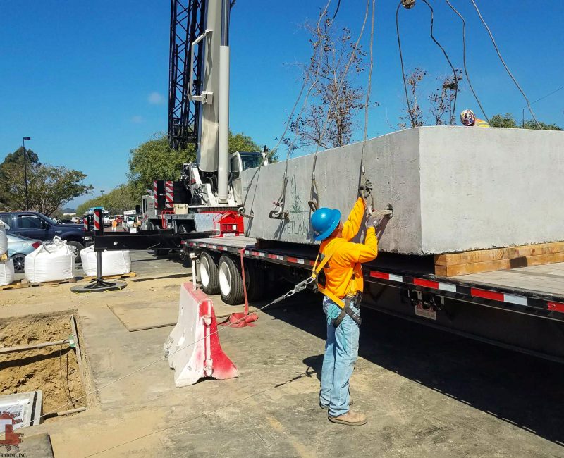 Worker guides concrete block onto trailer with crane.