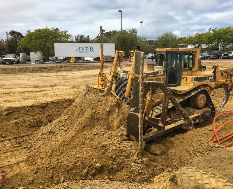 Yellow bulldozer moves dirt at a construction site, trucks nearby.