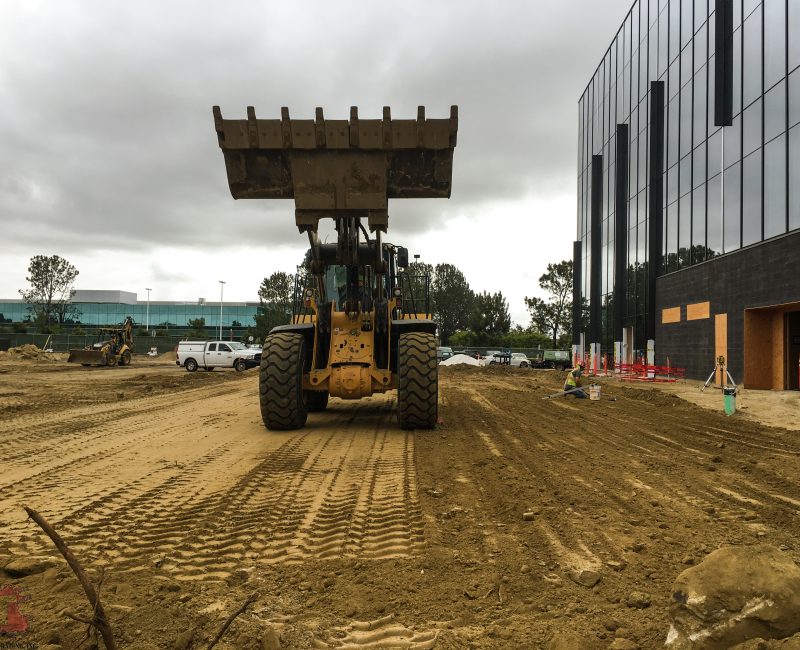 Yellow bulldozer on construction site near modern glass building.