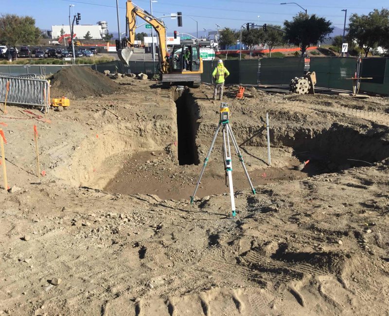 Construction site with excavator, worker, hole, equipment, and barriers.