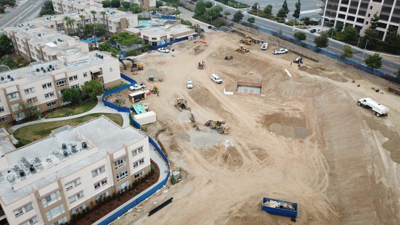 Aerial of construction site beside homes with vehicles and equipment.