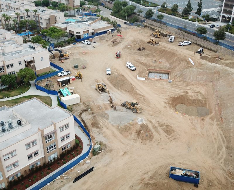 Aerial of construction site beside homes with vehicles and equipment.