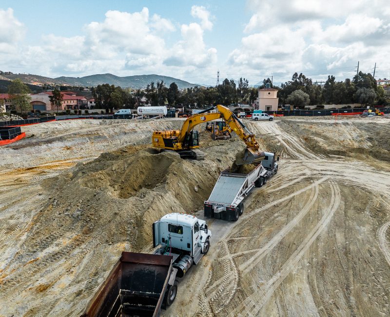 Excavator fills dump truck with soil at construction site.