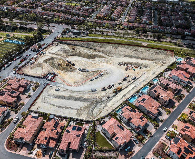 Aerial view of construction site amid red-roofed houses and fields.