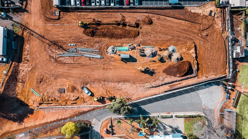 Aerial view: construction site, heavy machinery, dirt mounds, fencing.