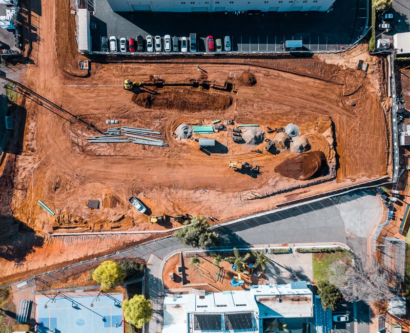 Aerial view: construction site, heavy machinery, dirt mounds, fencing.