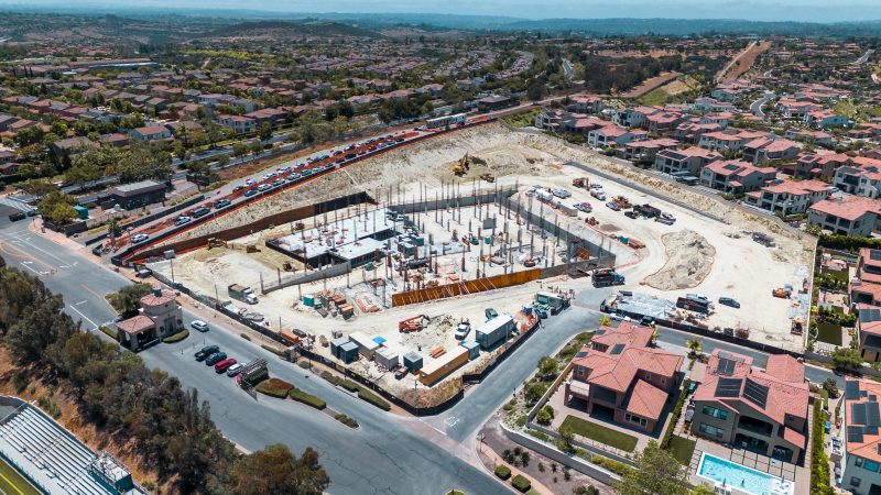 Aerial view of construction site with houses, beams, and vehicles.