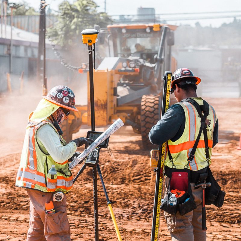 Workers survey site as yellow bulldozer operates behind them.