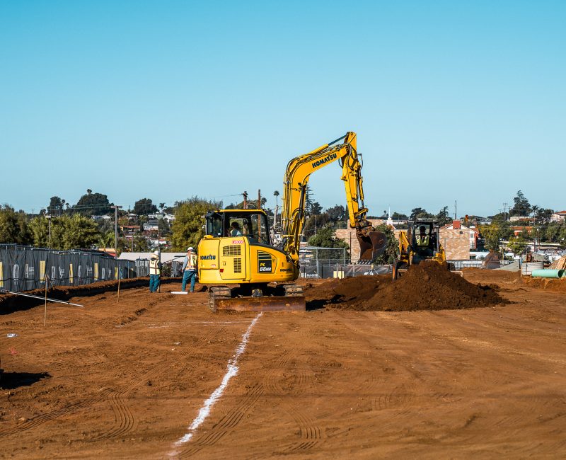 Two yellow excavators and two workers on a construction site.