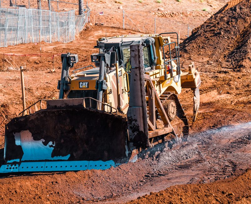 Yellow bulldozer pushes soil on reddish dirt construction site.