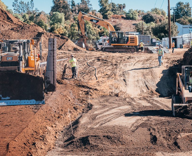 Three workers operate bulldozers and excavator at sunny construction site.
