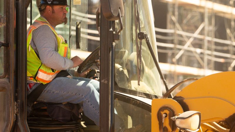 Worker in safety gear operates yellow vehicle at construction site.