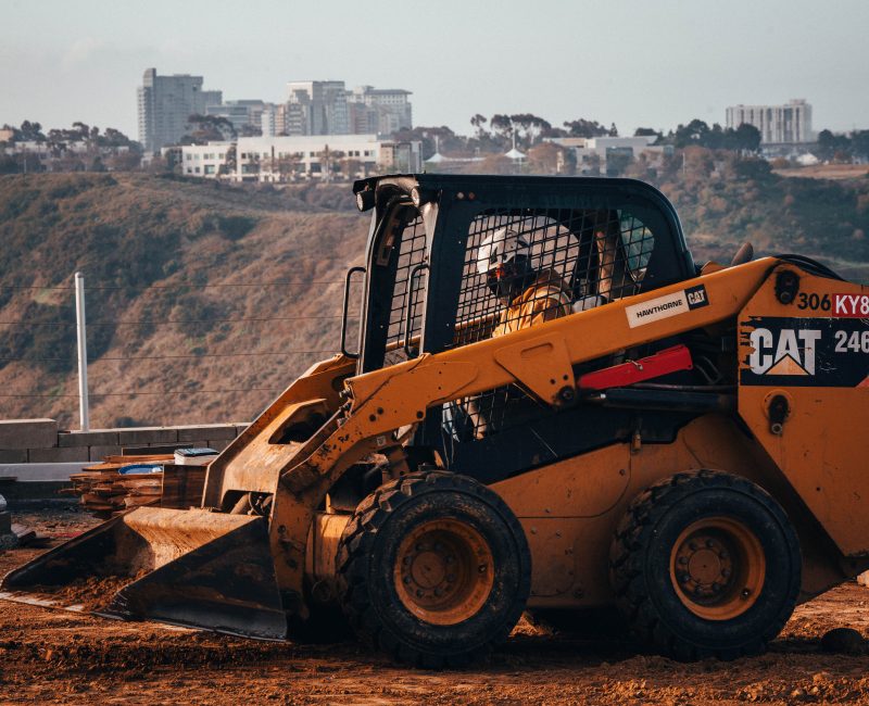 Yellow Caterpillar skid steer loader moves dirt on hillside site.