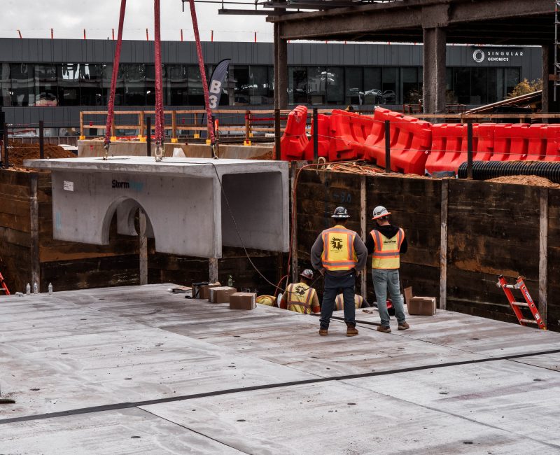 Two workers in safety gear stand on a construction site.
