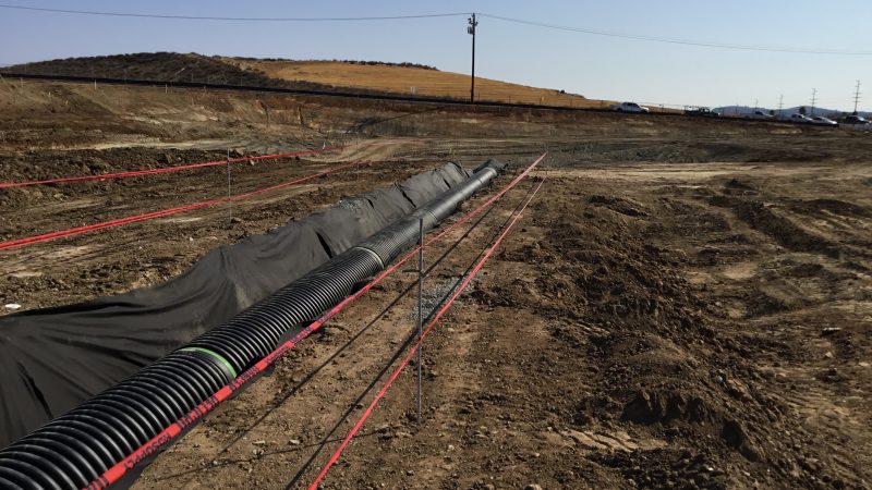 Black drainage pipes in fabric-lined trench, red tape nearby.