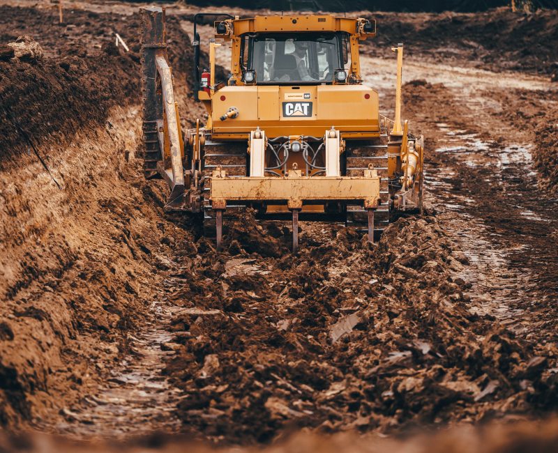 Yellow bulldozer digging a deep trench in muddy soil.