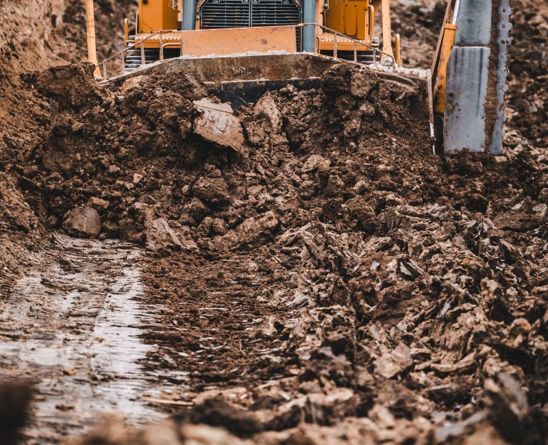 Yellow Caterpillar bulldozer moves dirt in muddy construction trench.