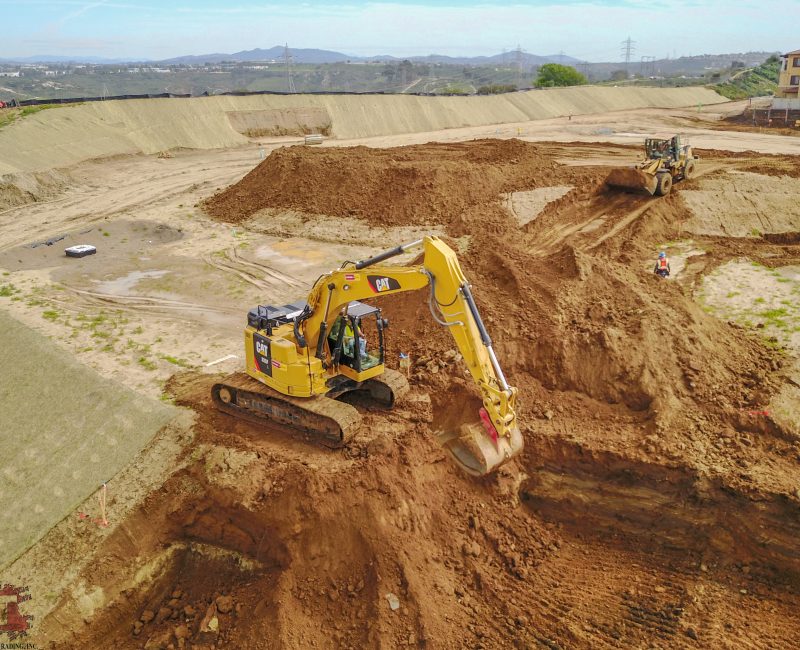 Yellow excavator and workers at large open construction site.