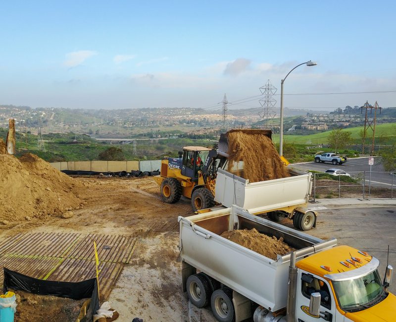 Bulldozers and dump trucks move dirt at a hilly site.