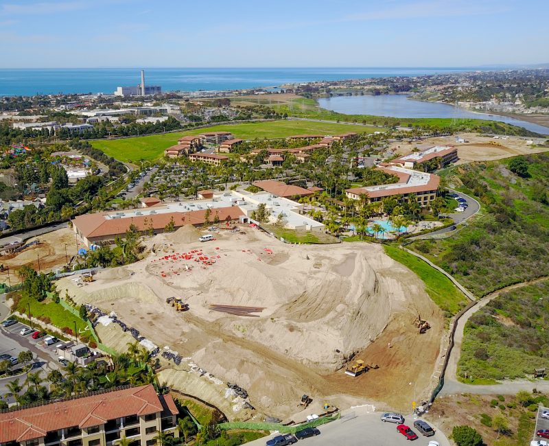 Aerial view of coastal construction site with nearby city and ocean.