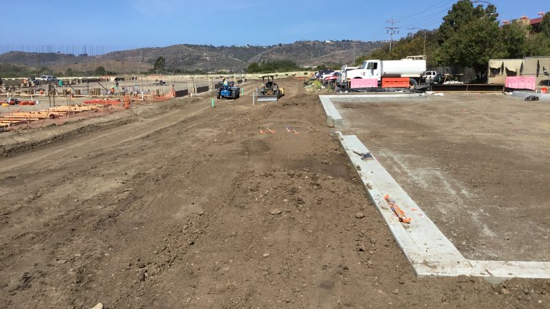 Construction site with machinery, workers, barriers, and hills.