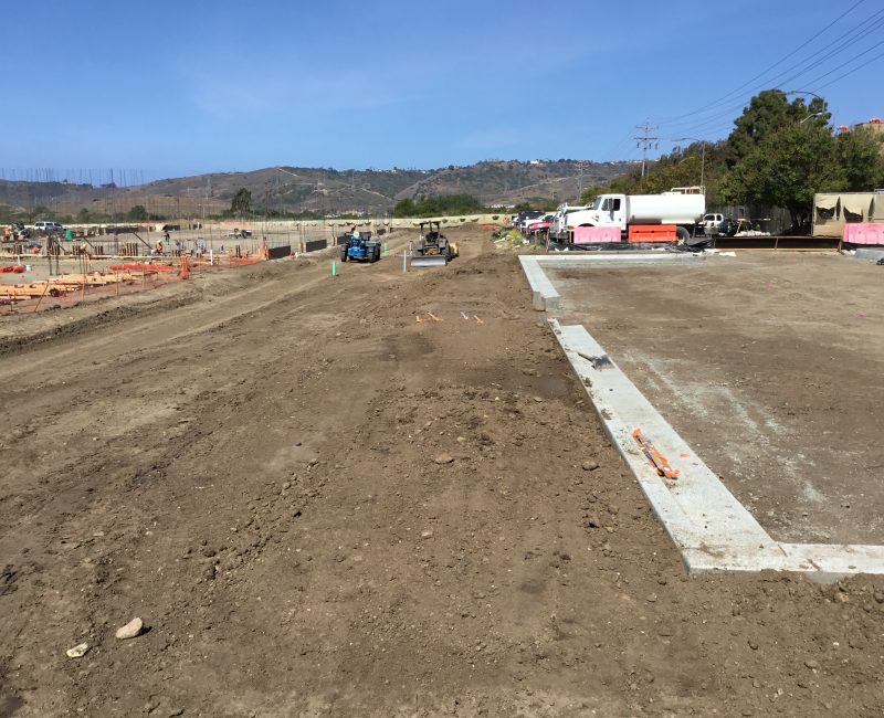 Construction site with machinery, workers, barriers, and hills.