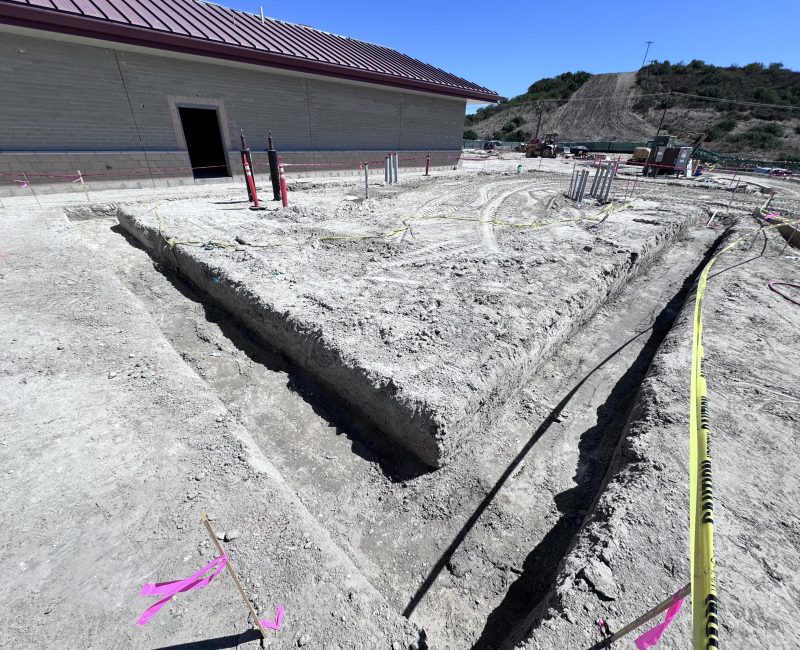 Dug trenches and pipes by a red-roofed building, clear sky.