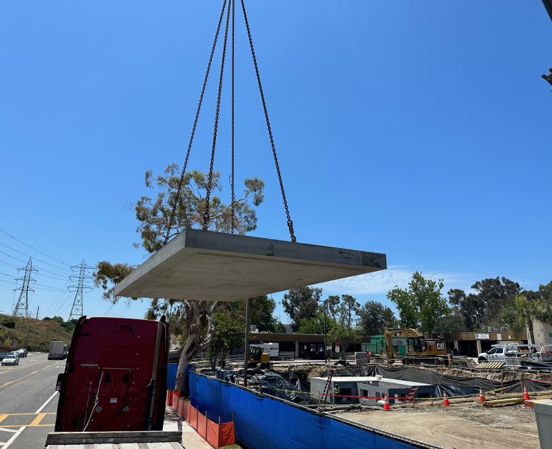 Crane lifts large concrete slab at sunny construction site.