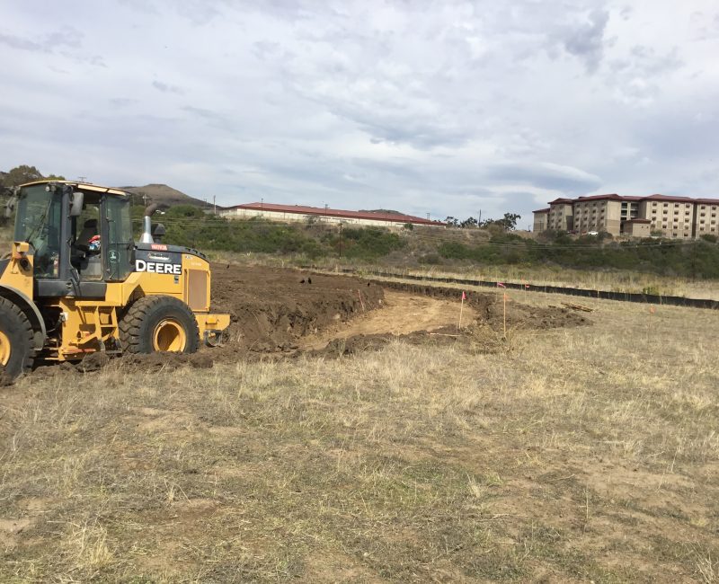 Yellow John Deere bulldozer moving dirt at grassy construction site.