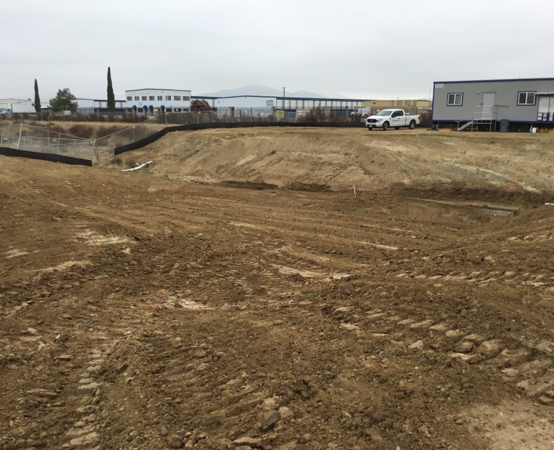 Muddy construction site with trailers, truck, and industrial buildings.