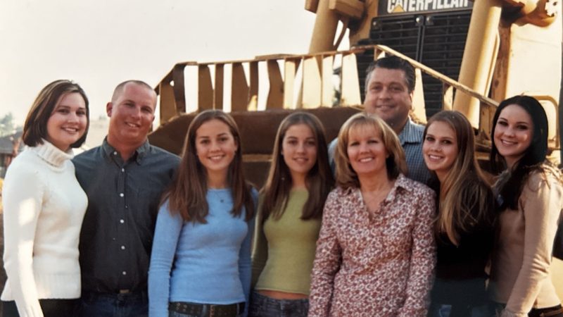 Seven people smiling by a Caterpillar construction vehicle outdoors.
